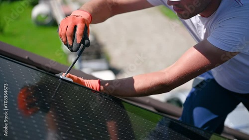 Worker building photovoltaic solar panel system on rooftop of house. Close up of man engineer in gloves installing solar module with help of hex key outdoors. Renewable energy generation concept. photo