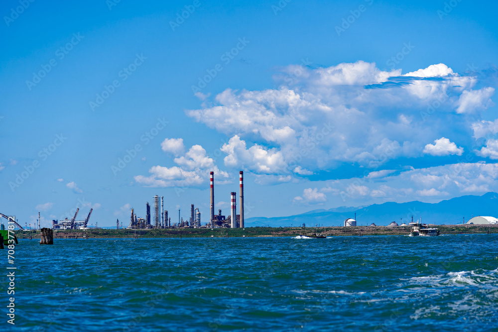 Scenic view of Mediterranean Sea with motorboat and chimneys of biorefinery in the background on a sunny summer day. Photo taken August 7th, 2023, Venice, Italy. Scenic view of Mediterranean Sea with motorboat and chimneys of biorefinery in the background on a sunny summer day. Photo taken August 7th, 2023, Venice, Italy.