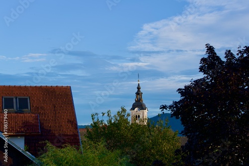 Church tower of Saint Ulrich church at village of Zabnica with trees and evening light with mountain panorama in the background. Photo taken August 7th, 2023, Zabnica, Kranj, Slovenia. photo