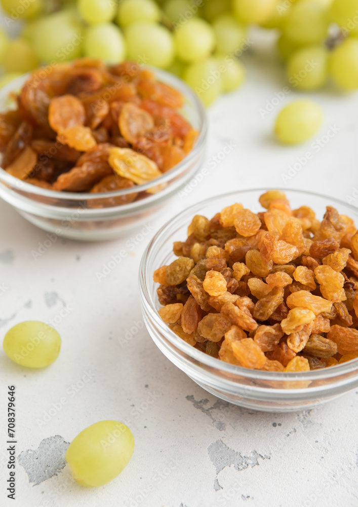 Dried sweet green raisins in glass bowl with ripe grapes on light kitchen background.Macro Dried sweet green raisins in glass bowl with ripe grapes on light kitchen background.Macro