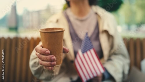 Senior female refugee holding U.S. flag and paper cup, asking for help, poverty photo