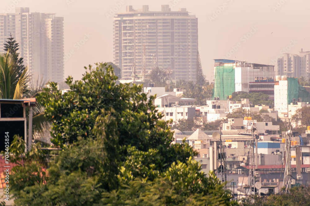 A hazy cityscape of modern concrete buildings beyond green trees.