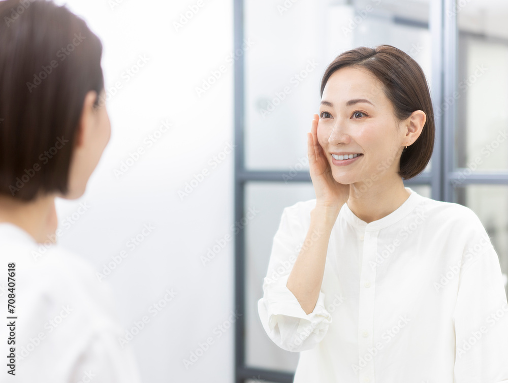 鏡を見ながら肌を触っているミドル世代の女性 鏡を見ながら肌を触っているミドル世代の女性