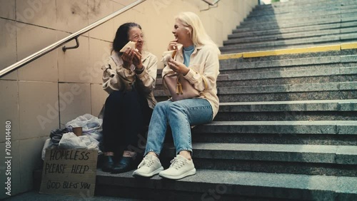 Thankful elderly homeless woman and woman passerby eating sandwiches, charity photo
