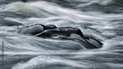 Schwarzer Stein im fließendem Wasser. Strömung umspühlt Steine. Fluß fließt um einen Steinhaufen herum.