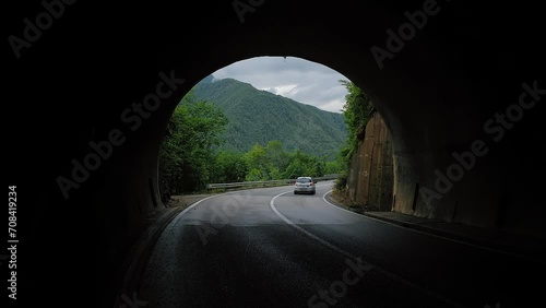 Car moving through mountain road tunnel exit, person emerges from the darkness photo