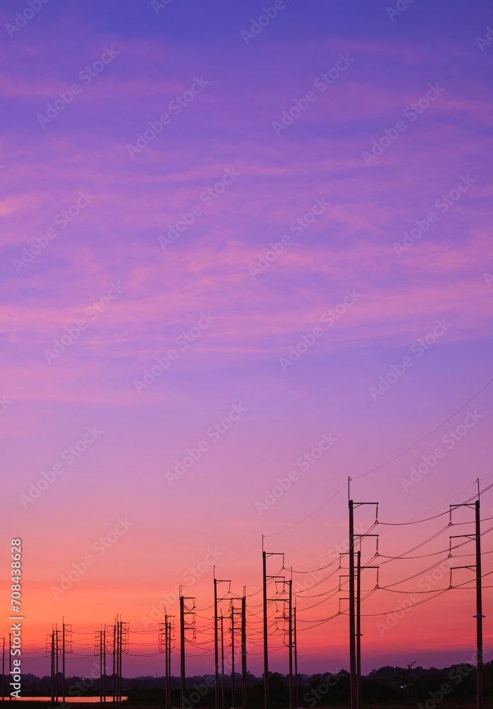 Silhouette row of electric poles with cable lines in countryside area against colorful twilight sky background in vertical frame