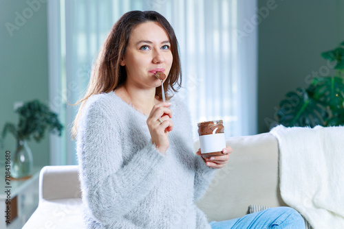 Young woman eating chocolate from a jar at home