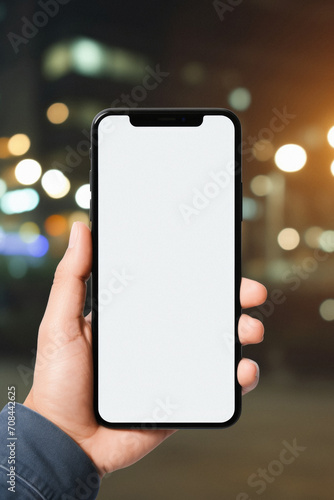 Mockup of a hand holding black mobile phone with blank white screen in the city at night