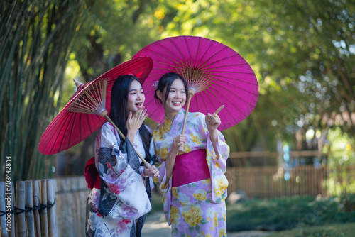 Pretty the Traveller Young Asian woman wearing a Japanese traditional kimono dress, a Yukata dress, and holding an umbrella is happy and cheerful in the green natural park.