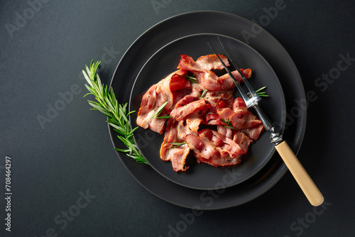  Roasted bacon slices with rosemary on a black plate. photo