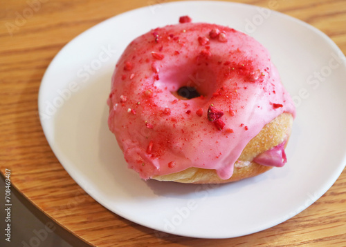 Mouthwatering strawberry glazed with raspberry cream filling doughnut on wooden table