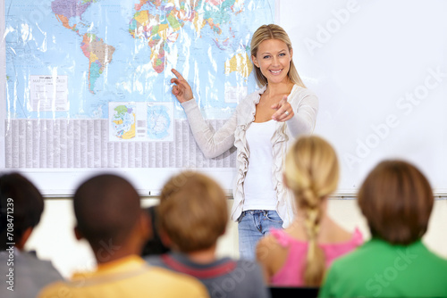 Teacher, geography and map in classroom with children, pointing and smile with test question. Person, teaching and talking to school kids for education, learning or development with quiz at academy