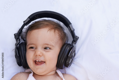 Baby, headphones and listening to song for fun, above and face on bed at home. Child, happiness and hearing audio for child development or learning, toddler and calming playlist for peace and calm