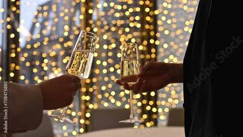 Close-up of a man and woman clinking glasses of champagne against the background of a golden garland