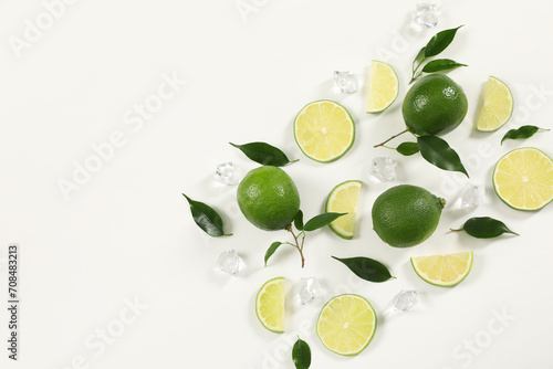 Limes, ice and green leaves on white background, flat lay. Space for text
