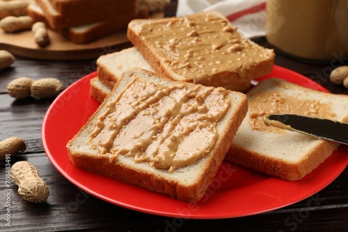 Delicious toasts with peanut butter, nuts and knife on dark wooden table, closeup
