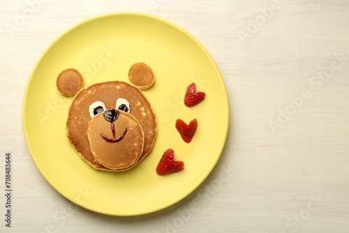 Creative serving for kids. Plate with strawberries, cute bear made of pancakes on light wooden table, top view Space for text