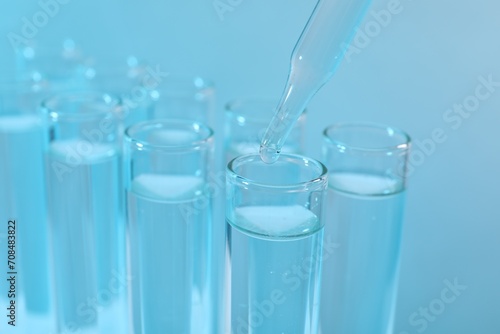 Laboratory analysis. Dripping reagent into test tube on light blue background, closeup