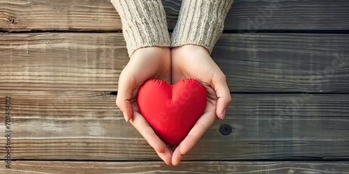 Hand of love and care. Human hands holding red heart symbol on wooden table symbolizing life health and support in concept of valentine day