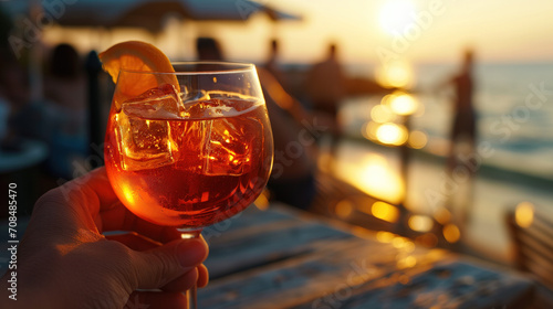 A close-up of an Aperol Spritz in the hand of a beach cafe visitor against the backdrop of the ocean.