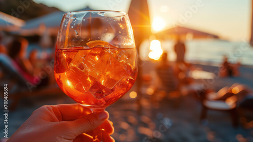 A close-up of an Aperol Spritz in the hand of a beach cafe visitor against the backdrop of the ocean.