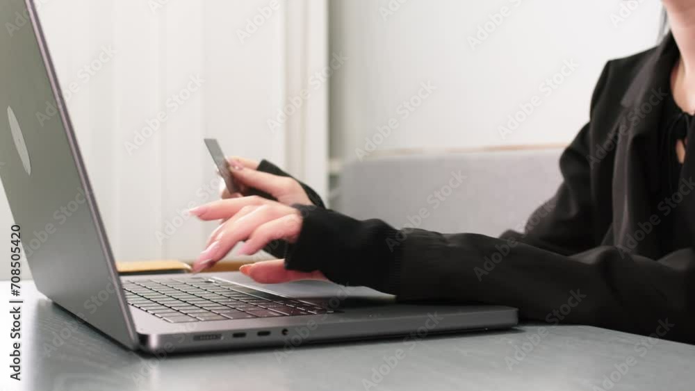 Close-up of a young woman's hands making online purchases through a laptop at a table in a room with a bank card. Online shopping and using credit cards concept. Close-up of a young woman's hands making online purchases through a laptop at a table in a room with a bank card. Online shopping and using credit cards concept.