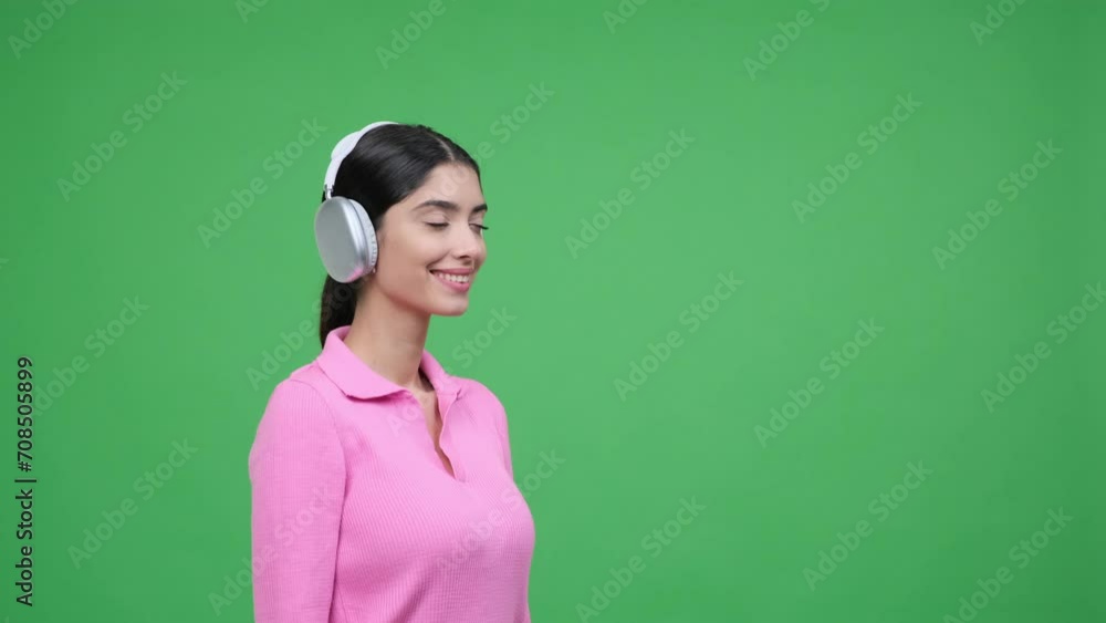 Woman wearing headphones gazes to the right, capturing a moment of curiosity or attention toward something off screen. Creating scene filled with a sense of focus and intrigue on green background. Woman wearing headphones gazes to the right, capturing a moment of curiosity or attention toward something off screen. Creating scene filled with a sense of focus and intrigue on green background.