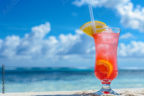 A colorful tropical drink garnished with an orange slice sits on a wooden ledge in front of a blue ocean.