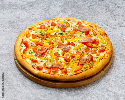 Homemade Italian style pizza with cheese, yellow and red peppers, bacon and tomatoes close-up on a wooden board on the table. Horizontal