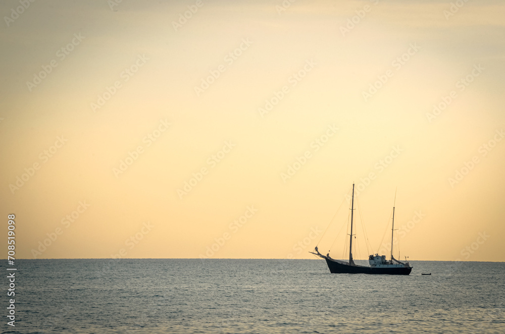 Yacht resting on sea water in sunset light with a tiny still visible plane rising from the nice airport