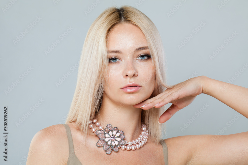 Blond fashion model woman with clear fresh perfect skin and long blonde hair wearing jewelry pearl necklace posing on gray studio background, fashion beauty portrait