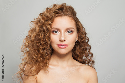 Beautiful young female model healthy woman with long wavy frizzy hairstyle and clear skin studio portrait. Hair care, facial treatment and cosmetology concept