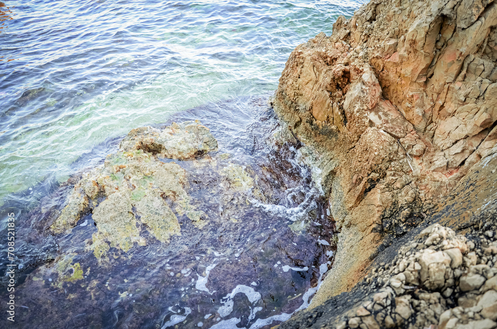 Rock textured cliff corner isolated in the blue sea calm waters on sunny day light