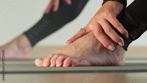Woman in leggings holding hands on feet during break of sport activity. Sporty woman exercises barefoot for strengthening ankle muscles photo