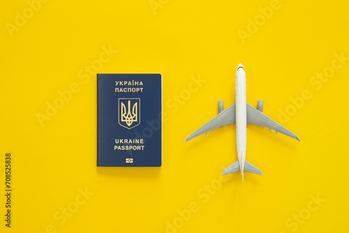 Fototapeta Naklejka Na Ścianę i Meble -  Ukrainian biometric passport, dollar bills and airplane figurine on a yellow background, top view. The concept of travel, migration and refugee from Ukraine.