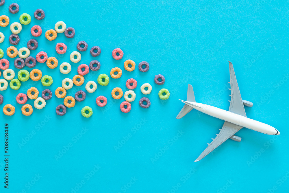 Colorful fruit corn rings and toy airplane on a blue background. Children breakfast option with cornflakes. Flat lay.