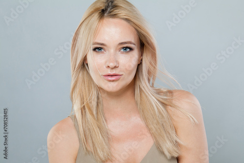 Perfect smiling joyfully female model with fair hair looking at camera, being happy. Studio shot of good-looking beautiful woman with pure shiny skin and blonde hair on gray background