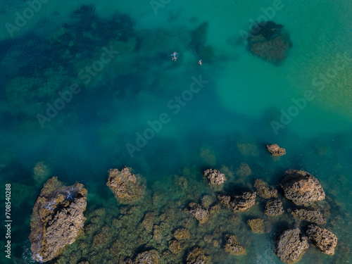 Two snorkelers swimming in turquoise sea near the rocks in Malta aerial top down. Perfect summer holidays activity.