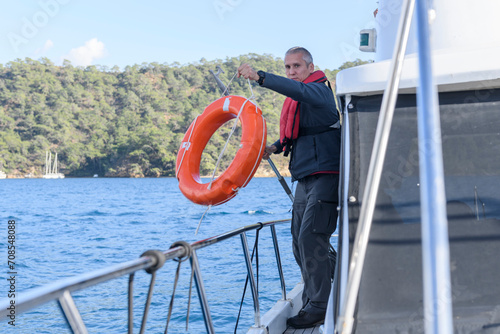Young caucasian man with life buoy. Motor boat captain. Man over board. Yachting concept. Man wearing inflatable life jacket.