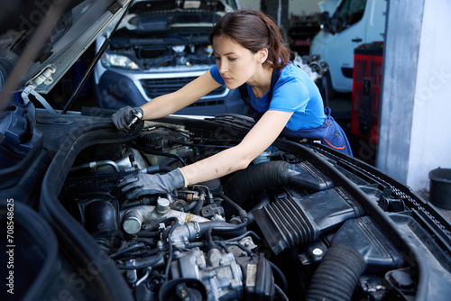 Charming young female mechanic inspects engine under hood of car