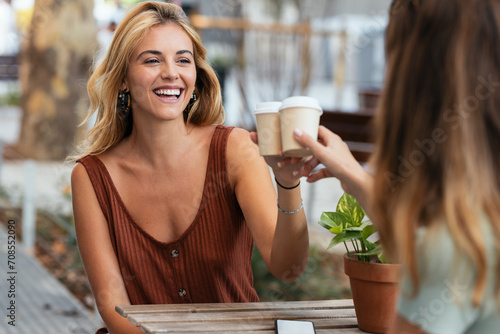 Two attractive friends enjoying coffee together while talking and laughing sitting on the terrace of a bar.