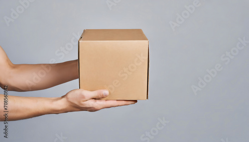 Side profile close up of hand holding carton craft paper parcel on gray background with copy space photo