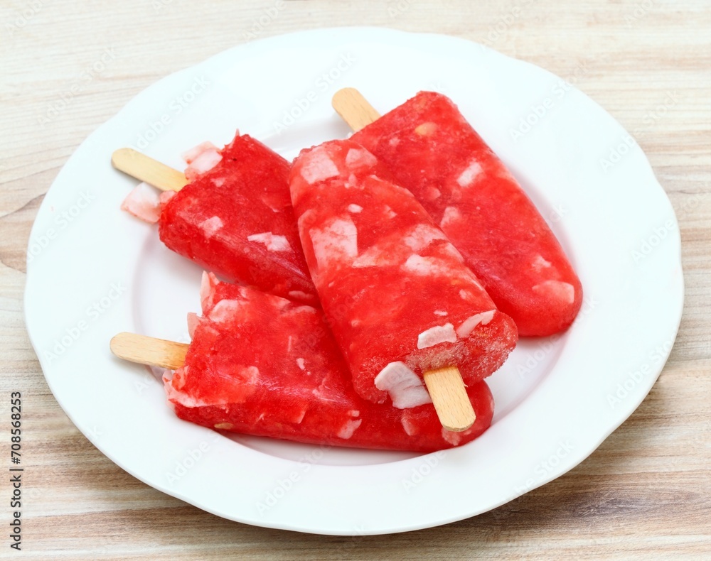 Homemade ice lolly from water melon with almond pieces. Delicious fruit popsicle with the stick on the plate.
