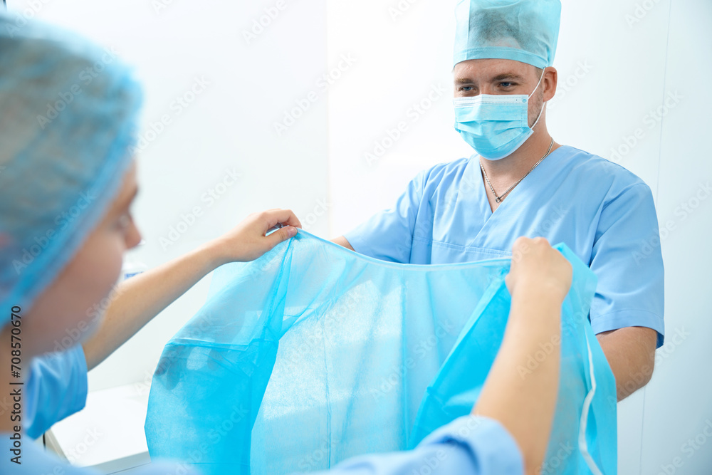 Fototapeta premium Cropped female nurse helping male doctor put on medical gown before surgery