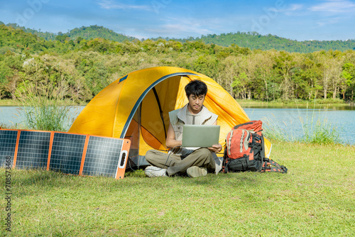 Young Asian man working busy while in outdoor lifestyle camping in forest mountain using computer notebook laptop and solar cell