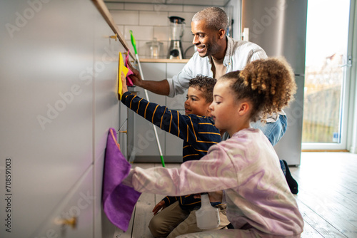 Smiling father cleaning kitchen with children at home
