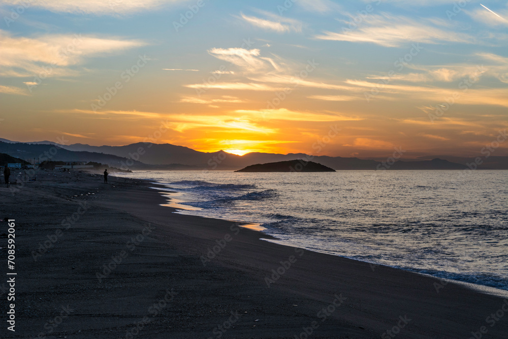 Fototapeta premium Sunset at the beautiful beach, Wooden tree trunk on the sea coast with sunset, sky and clouds, view from Sea landscape in the Mediterranean sea in Jijel Algeria Africa, golden sunlight.