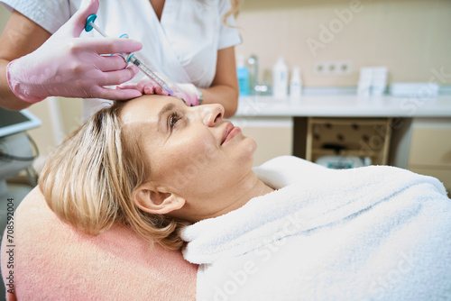 Cropped female beautician doing face beauty injection with syringe of woman