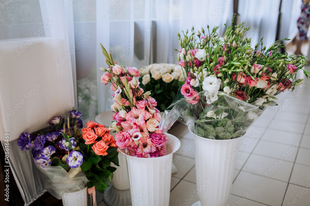 Plastic white vases with multi-colored flowers in packages stand in the restaurant. Photography, birthday gifts.